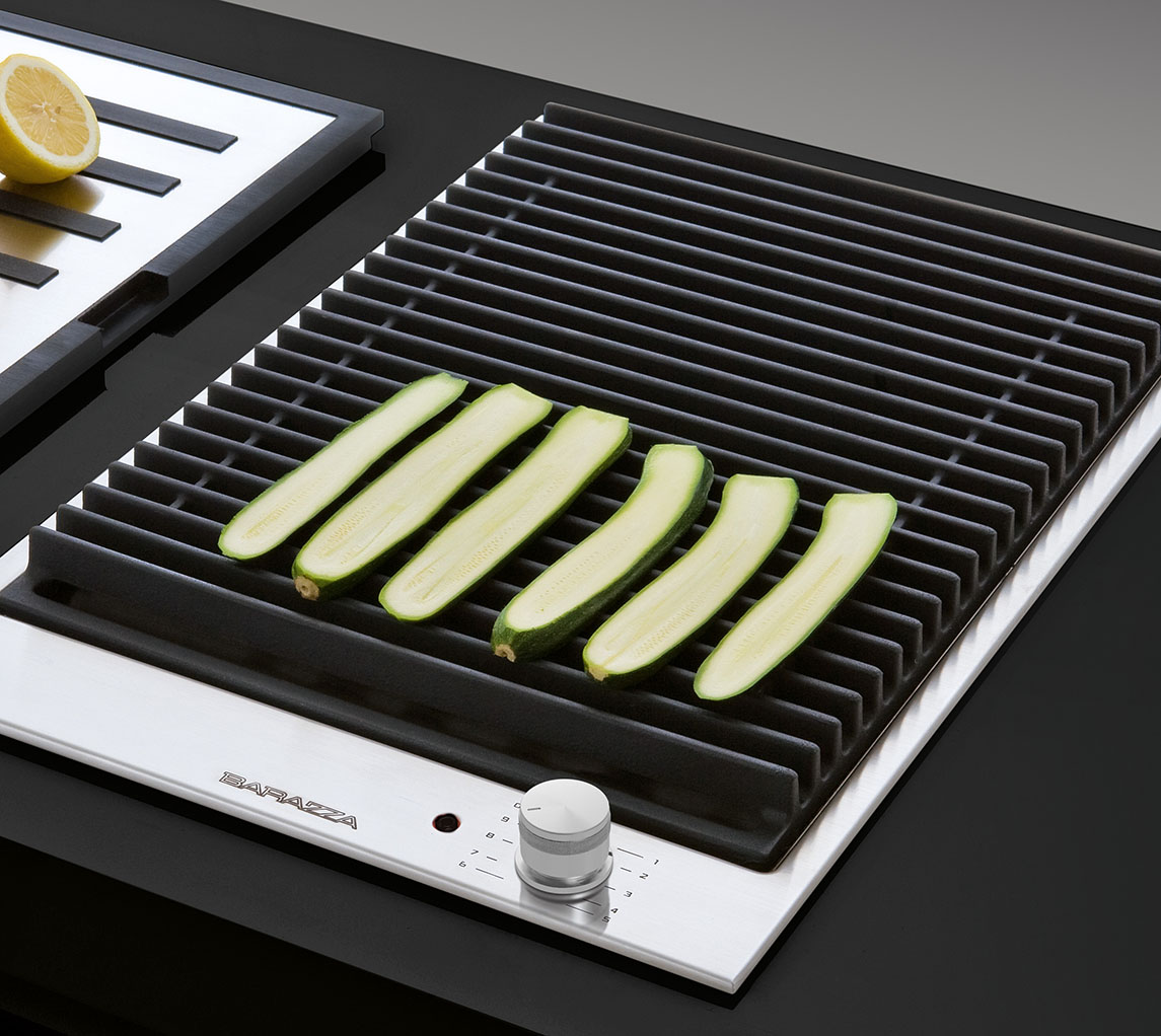 Delle zucchine tagliate verticalmente sono posate su una griglia in ghisa appartenente ad un piano di cottura adatto alla modalità barbecue