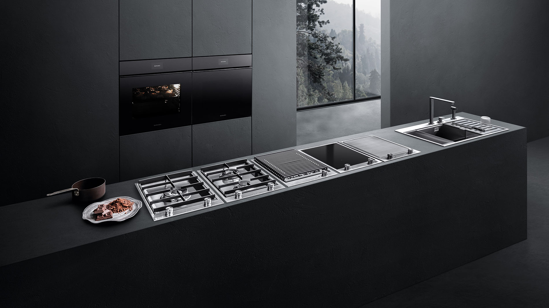 Vista di una cucina dotata di vari piani cottura, lavello a vasca quadra con accessori e due forni a incasso. Sullo sfondo c'è una finestra con vista sul paesaggio esterno