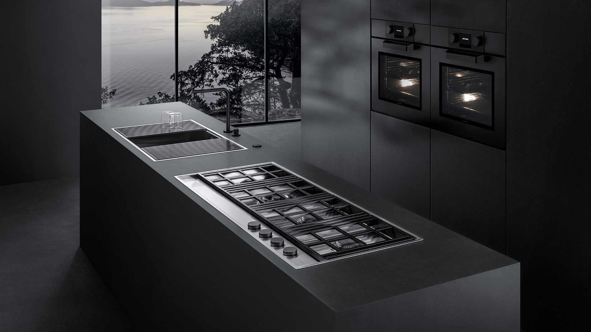 Vista di una cucina con due forni sullo sfondo e, in primo piano, un piano cottura a gas che si affianca a un lavello con griglie di sgocciolamento.