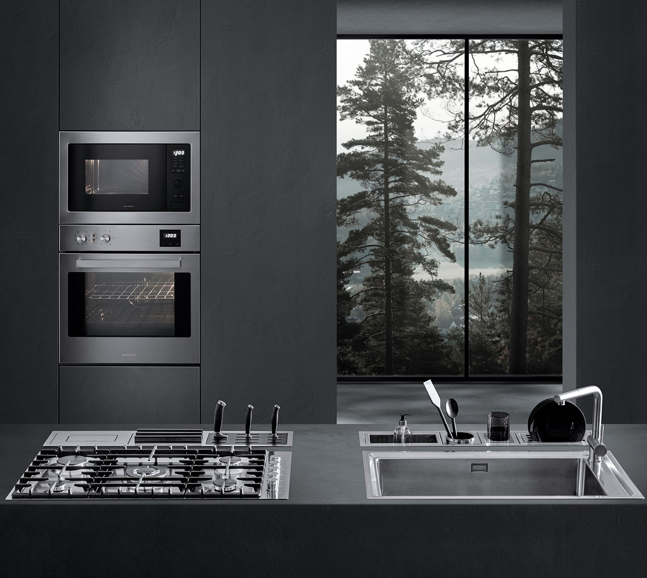 Vista di una cucina dotata di piano cottura a gas, lavello a vasca quadra, canali attrezzati con vari accessori e due forni a incasso. Sullo sfondo c'è una finestra con vista sul paesaggio esterno