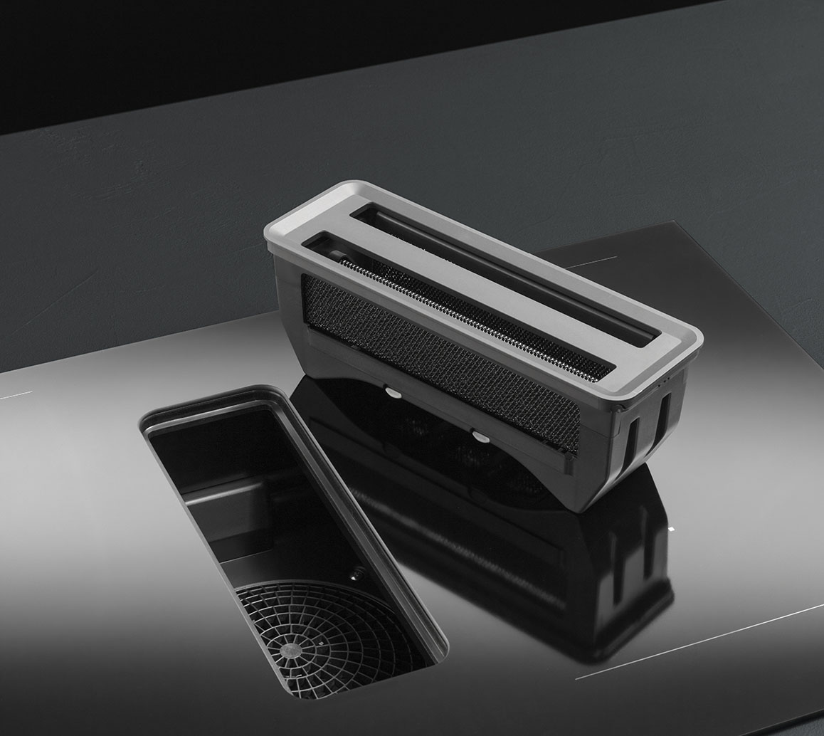Dettaglio di un piano a induzione con cappa aspirante integrata dal quale è stato rimosso il filtro che ora poggia sul piano stesso