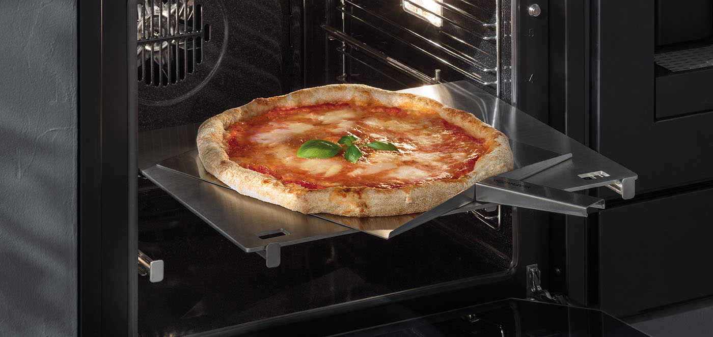 Forno con sportello aperto contenente piastra e pala per pizza in acciaio inox sulla quale è poggiata una pizza margherita