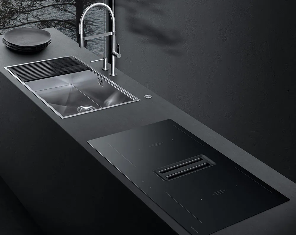 Piano da cucina su cui si affiancano un piano ad induzione in vetroceramica nera con cappa aspirante integrata e un lavello in acciaio inox a vasca quadra con accessorio