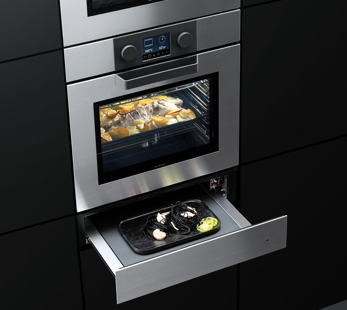 Vista di un forno ad incasso contenente del cibo in cottura sotto il quale si può notare un cassetto scaldavivande aperto sul quale poggia un piatto.