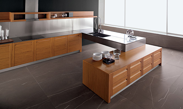 Vista di una cucina in legno composta da due piani montati su armadietti, sui quali sono poggiate delle stoviglie, che sorreggono un piano in acciaio sul quale è incassato un lavello a vasca quadra.Su uno dei piani è montato un piano a induzione sormontato da una cappa aspirante