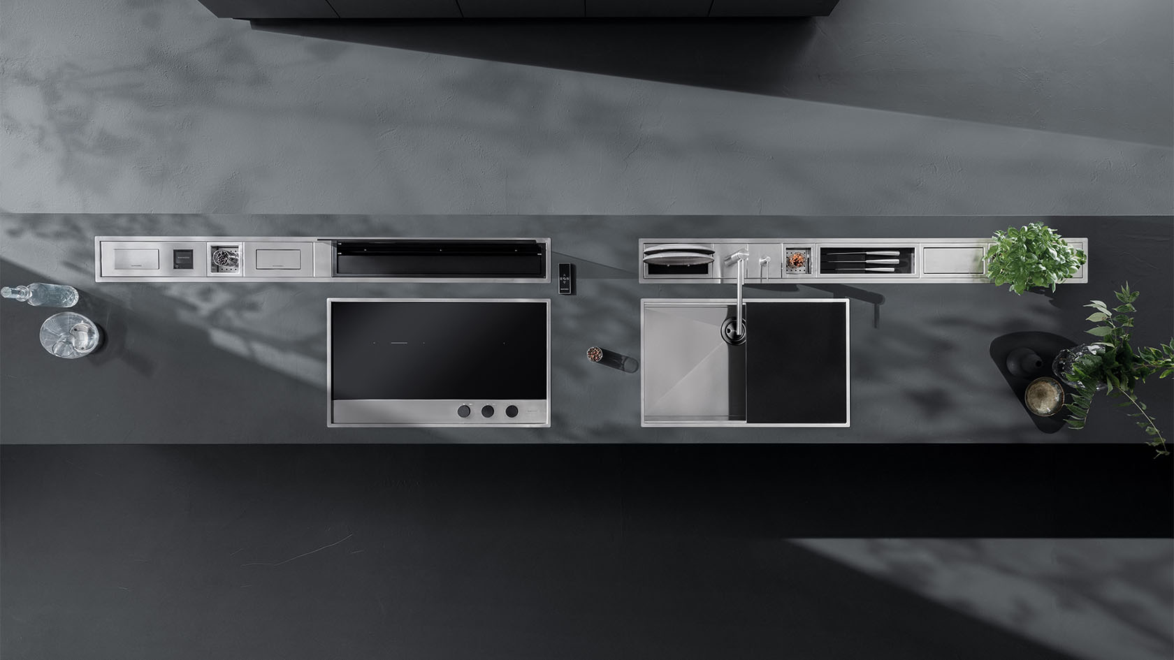 Vista aera di un piano dotato di piano cottura a induzione, lavello a vasca quadra e sopra ai quali si possono notare due canali attrezzati con diversi accessori.
