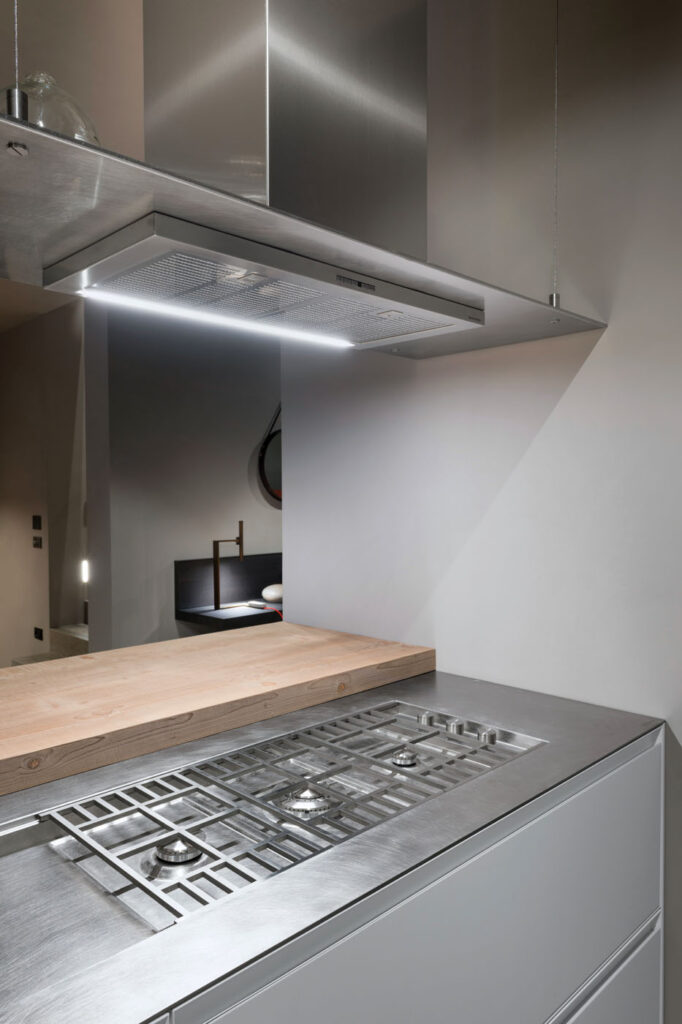 Dettaglio di una cucina dove si può notare un piano cottura a gas in acciaio, sormontato da una cappa aspirante, davanti al quale è posto un piano in legno.
