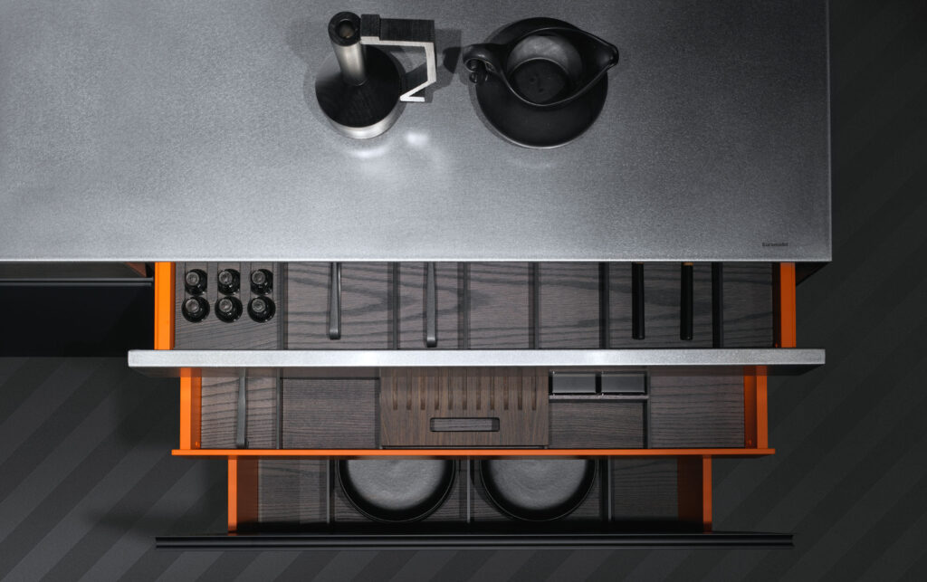 Dettaglio di un mobile a cassettiera aperto che mostra i contenuti dei vari cassetti, quali stoviglie e accessori per cucina vari