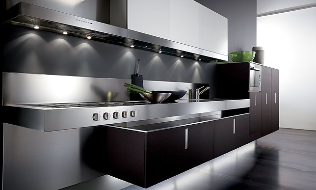 Cucina a parete composta da un piano in acciaio con lavello e piano cottura, sormontato da una cappa aspirante, e del mobilio in legno scuro nel quale è incassato un forno e sul quale poggiano degli oggetti decorativi