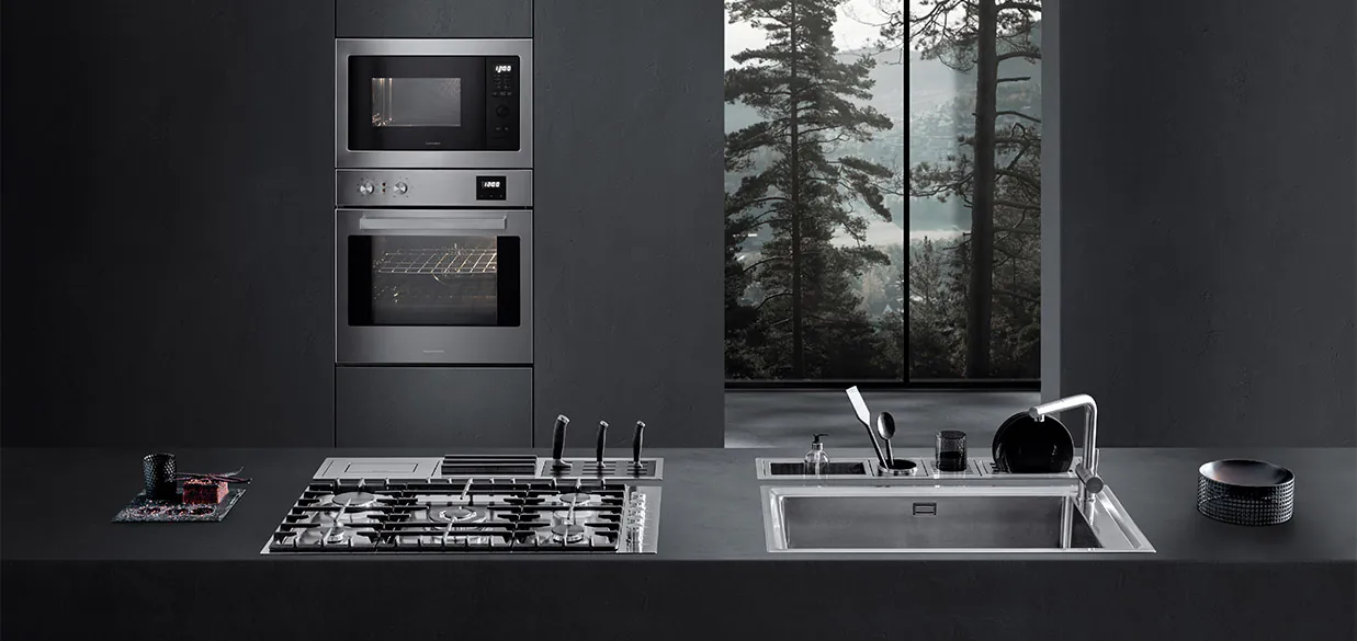 Vista di una cucina dotata di piano cottura a gas, lavello a vasca quadra, canali attrezzati con vari accessori e due forni a incasso. Sullo sfondo c'è una finestra con vista sul paesaggio esterno.