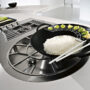 Dettaglio di un piano da cucina che mostra un wok in ghisa contenente del riso che poggia su un piano cottura in acciaio diviso in due fuochi dalle forme geometriche diverse