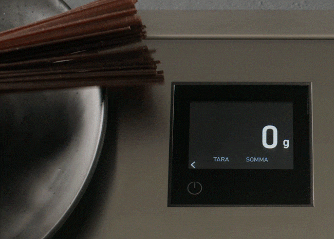 Spaghetti vengono pesati su una bilancia a incasso che ne mostra il peso crescente.